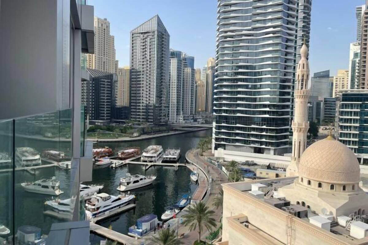 A high-rise building with a modern design, a marina with boats, and a mosque with a dome.