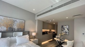 Una habitación de hotel moderna con cama, mesita de noche, lámpara y un área de comedor con mesa y silla.