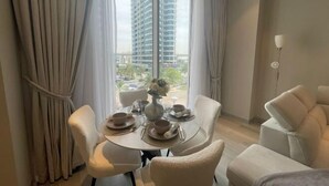 Un comedor con una mesa preparada para cuatro personas, un sofá y vistas a un edificio alto a través de amplias ventanas.