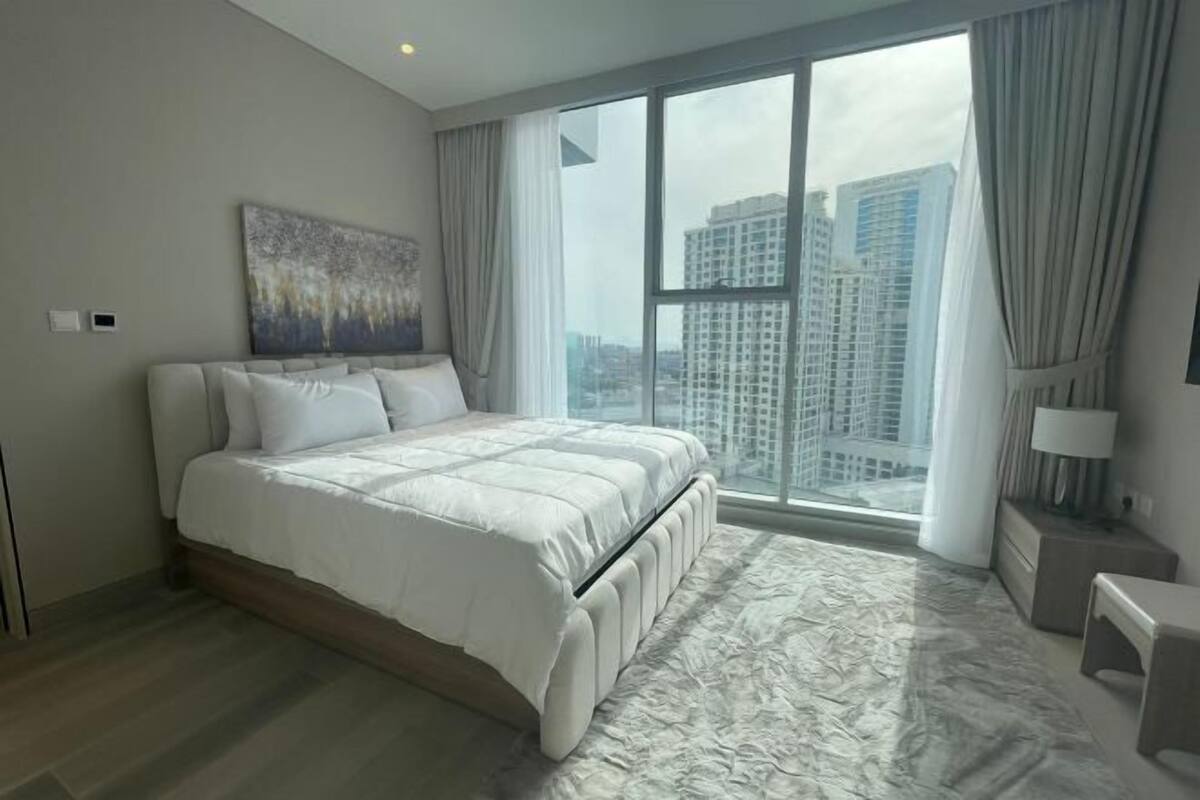A modern bedroom with a large bed, a city view, and a painting on the wall.