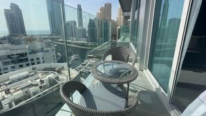 Un balcón en un edificio alto con barandilla de vidrio, sillas de mimbre y una mesa de cristal.