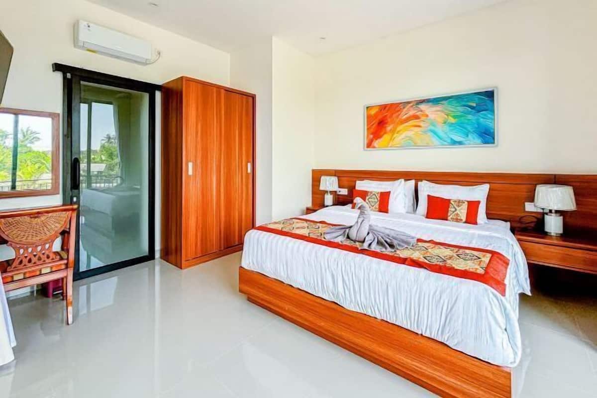 A modern hotel room with a large bed, wooden wardrobe, and a glass door leading to a balcony.