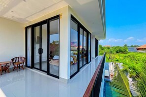 A modern balcony with a glass door, a small table, and chairs, overlooking a lush green landscape. - Dajan Dukuh Villa (2 Bedroom Villa with Minimum Stay 2 Night) (Bali)