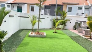 A well-maintained courtyard with artificial grass, palm trees, and a stone planter. - Stylish Blue Water Home w/ Pool (Tebrau)