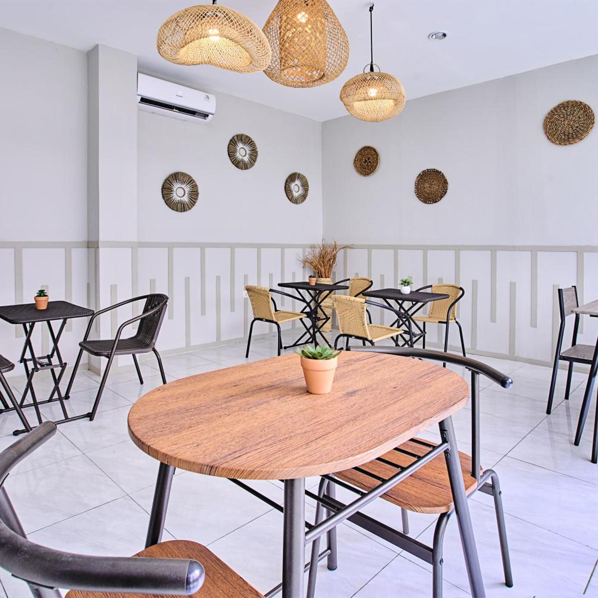 Un comedor moderno con mesas redondas, sillas de metal negro y lámparas colgantes tejidas.