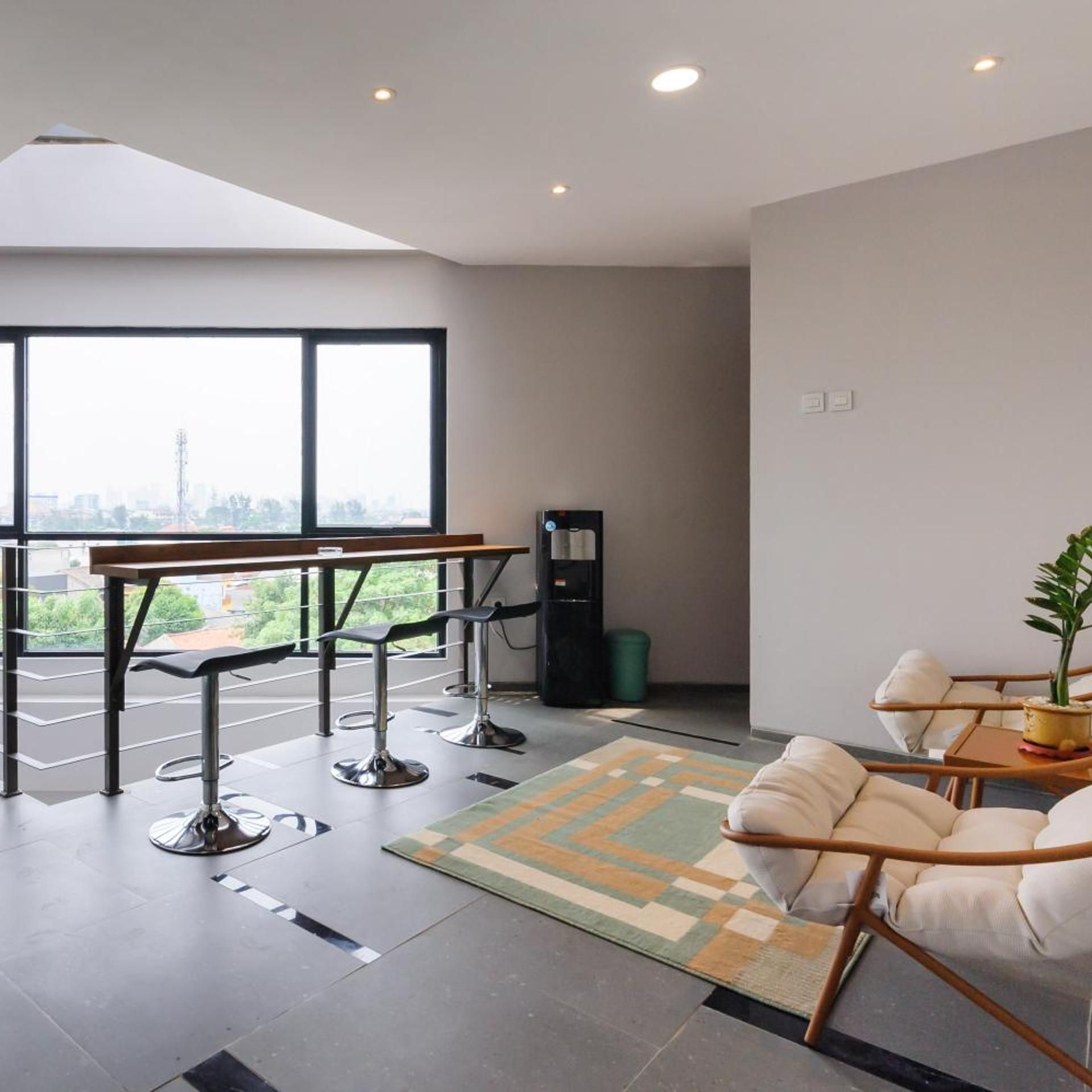 A modern interior with a high ceiling, a large window offering a city view, a bar area with stools, and a seating area with a patterned rug.