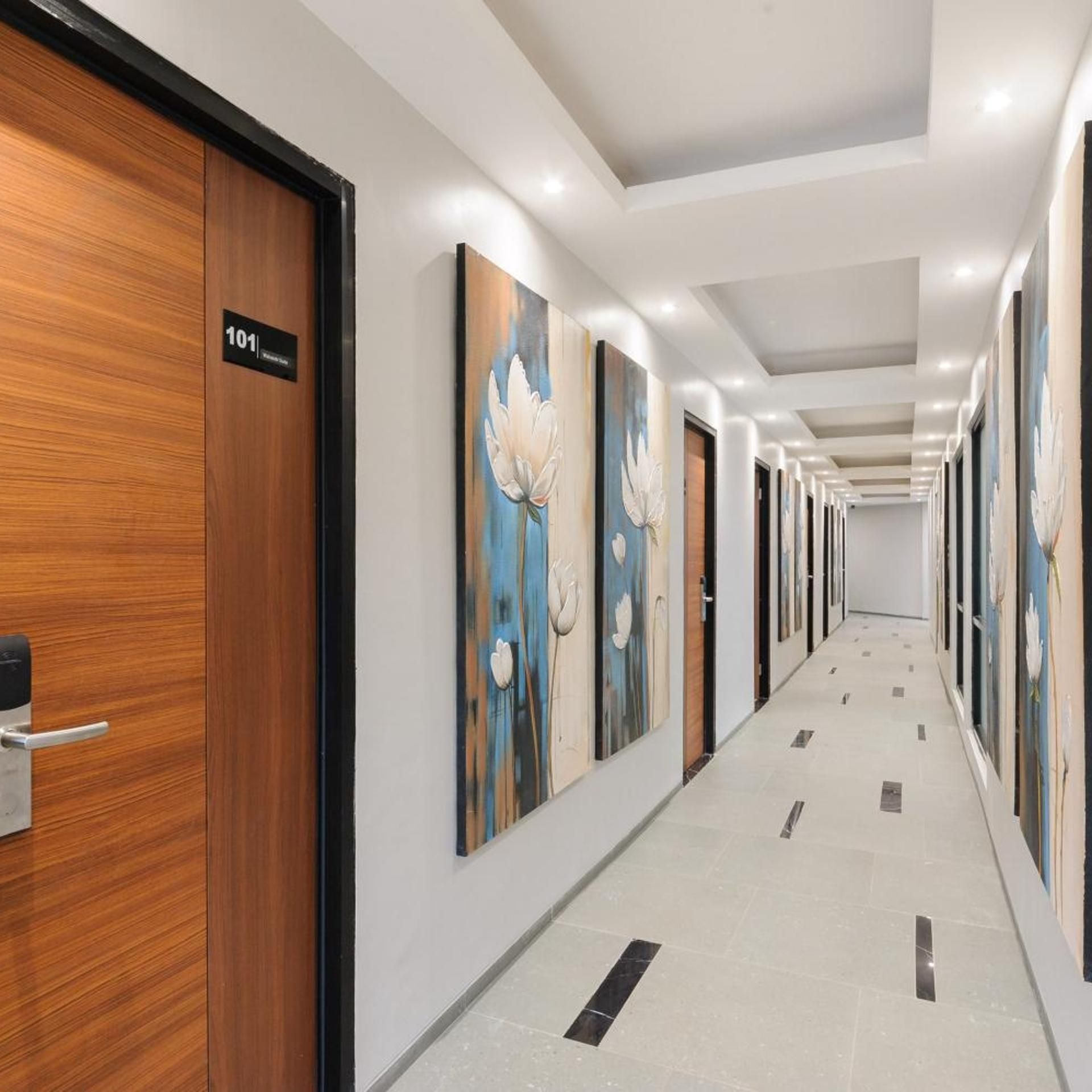 A hotel corridor with wooden doors, numbered room signs, and floral artwork on the walls.