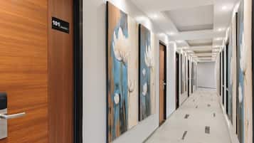 A hotel corridor with wooden doors, numbered room signs, and floral artwork on the walls.