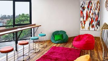 Un espacio moderno para vivir con piso de madera, un tapete rojo, un sillón de cuentas verde y un cuadro abstracto de colores en la pared.