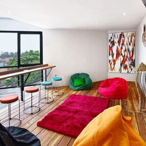 A modern living space with a wooden floor, a red rug, a green bean bag chair, and a colorful abstract painting on the wall. - Bale Puri (West Jakarta)