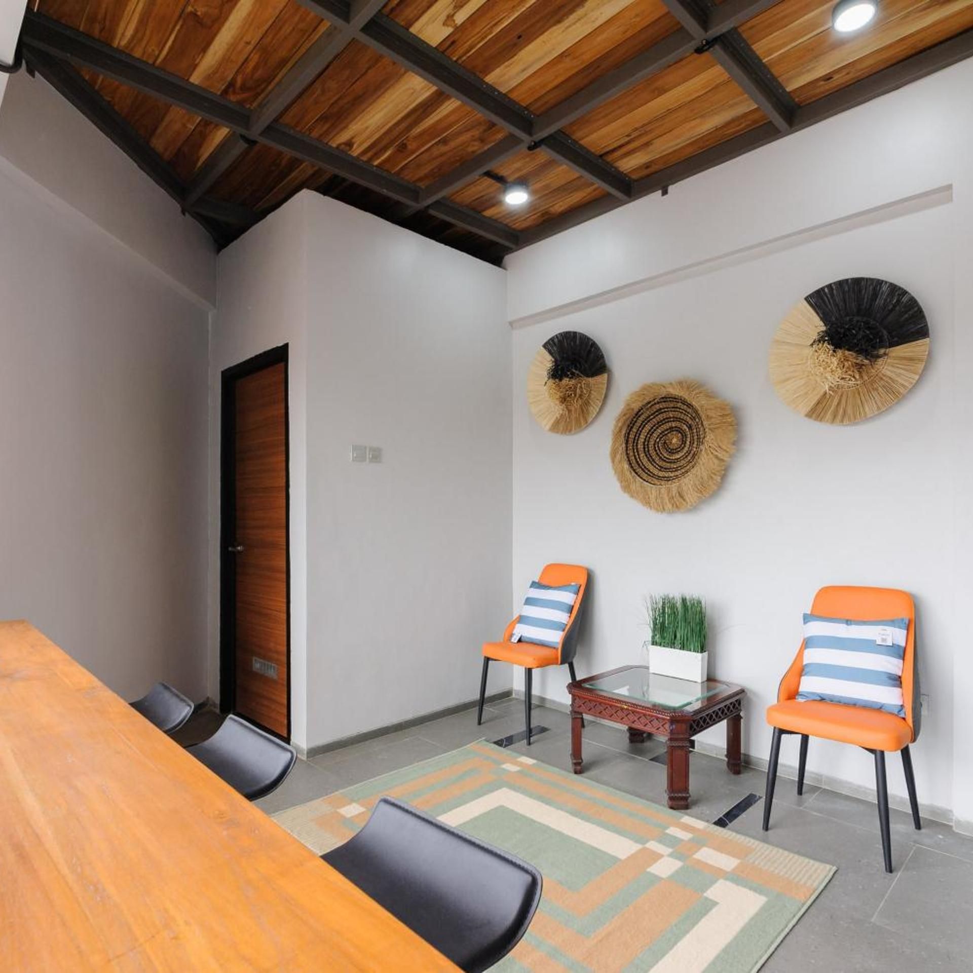 A conference room with a wooden table, two chairs, a small table with a plant, and decorative wall fans.