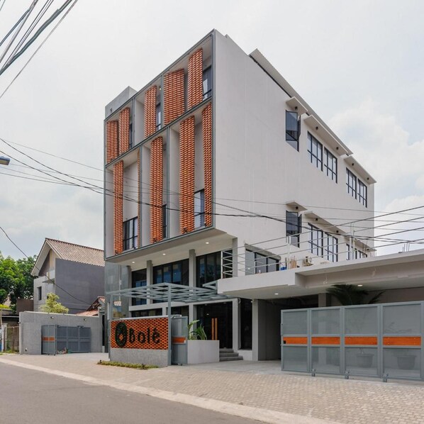 A modern building with a glass entrance, a sign with a logo, and a parking area. - Bale Puri (West Jakarta)