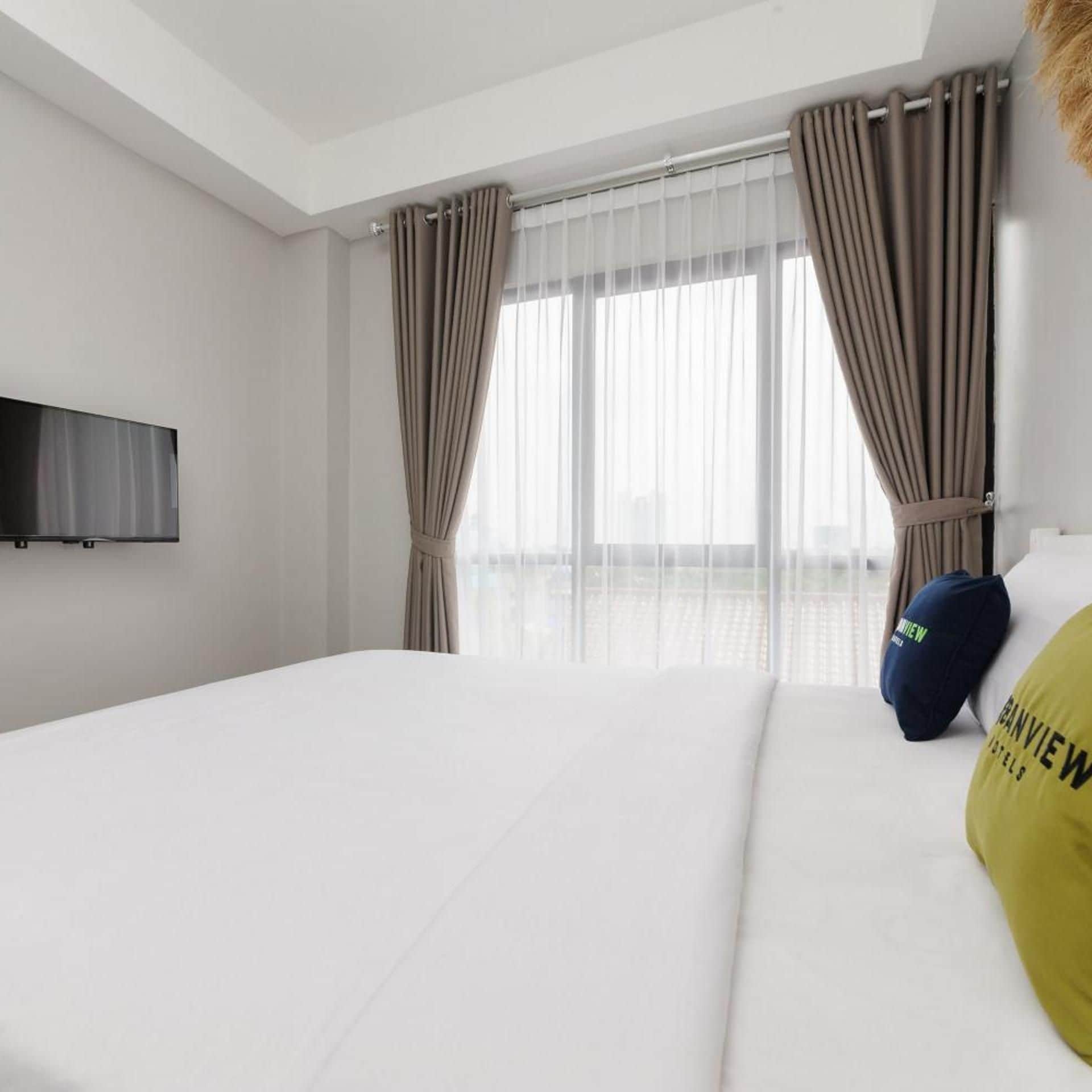 A hotel room with a bed, curtains, a TV, and a city view.