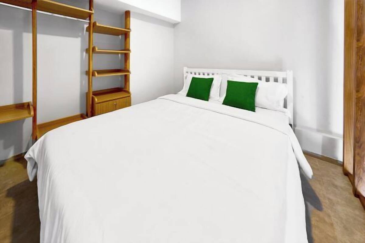 Un dormitorio con cama blanca, almohadas verdes, una escalera de madera y un armario blanco.