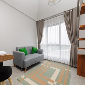 A modern room with a grey sofa, green cushions, a wooden side table, and a patterned rug. - Bale Puri (West Jakarta)