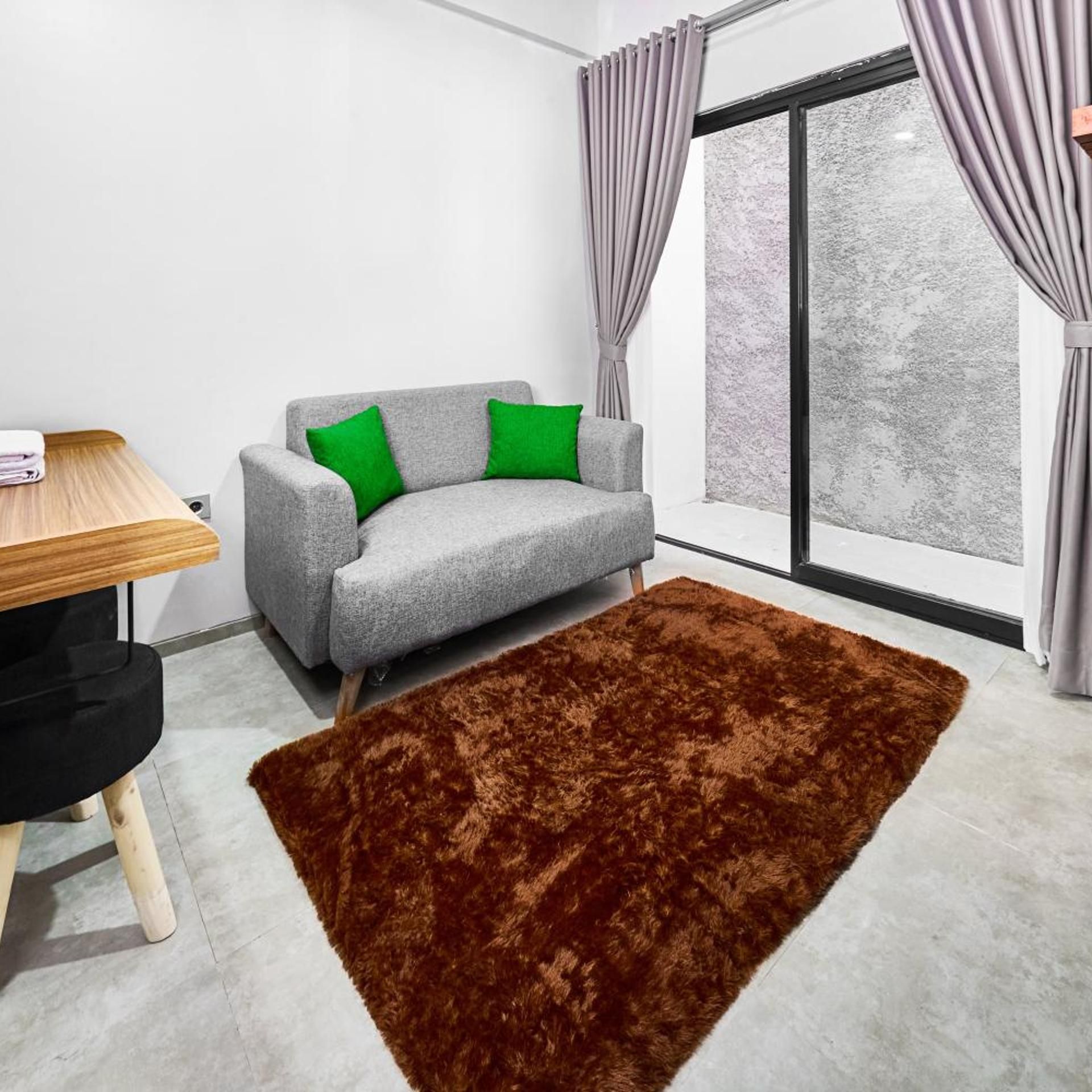 A modern living room with a grey sofa, green cushions, a wooden table, and a brown rug.