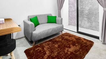 A modern living room with a grey sofa, green cushions, a wooden table, and a brown rug.