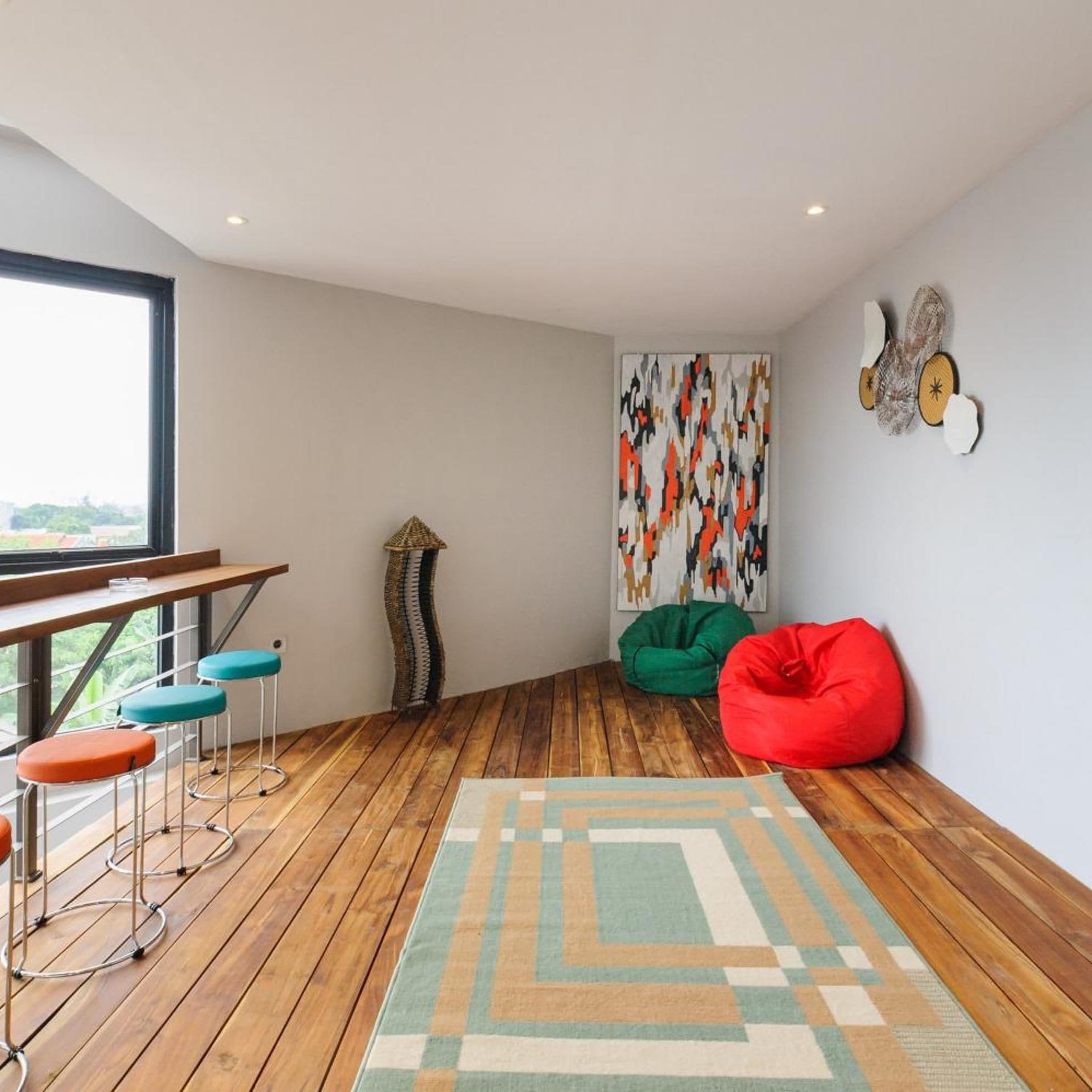A modern interior with a wooden floor, a dining area with stools, a green and red bean bag, and a colorful abstract painting.