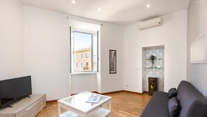 A modern living room with a flat-screen TV, a glass-top coffee table, a dark sofa, and a fireplace with a decorative mantle. - Rental in Rome Ripa Apartment (Rome)