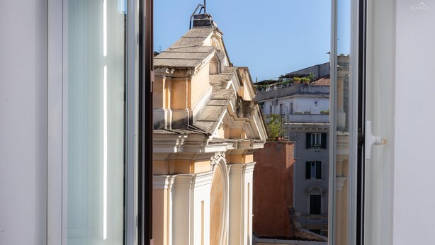 A view through a window of a building with classical architecture, including ornate detailing and a pitched roof. - Rental in Rome Ripa Apartment (Rome)