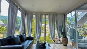 A modern living room with a black sofa, a coffee table with a plant, and large windows with curtains. - 217 Casa Del Mar Pool Villa@Casa Sakoo Phuket (Phuket)