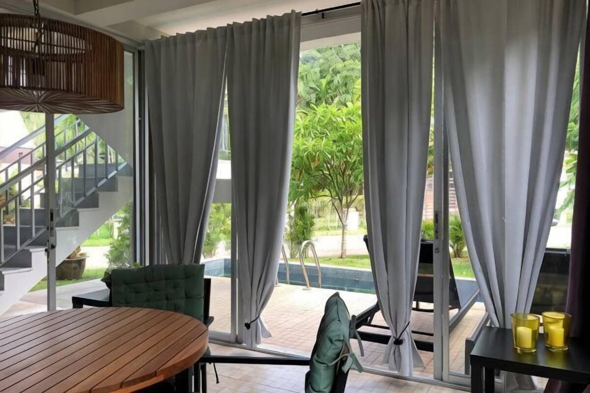 Quarto com mesa de madeira, uma cadeira verde, escada e vista para o verde lá fora.