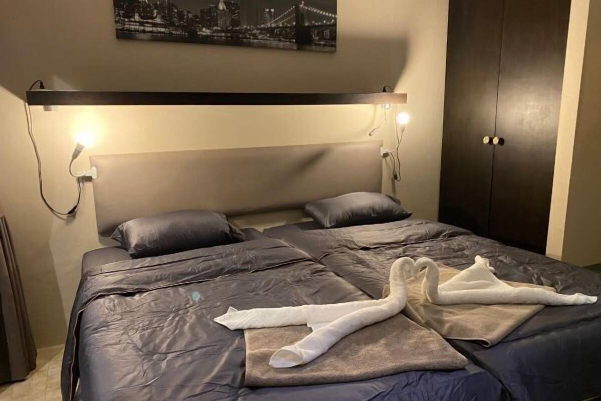 Quarto de hotel com cama, cabeceira iluminada, porta escura e quadro com vista para a cidade na parede.