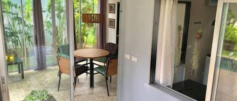 A room with a sliding glass door leading to a balcony, a round table with chairs, and a hanging plant.