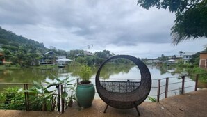 A circular metal chair with a metal stand, a green pot, and a railing overlooking a body of water with houses in the background. - 217 Casa Del Mar Pool Villa@Casa Sakoo Phuket (Phuket)