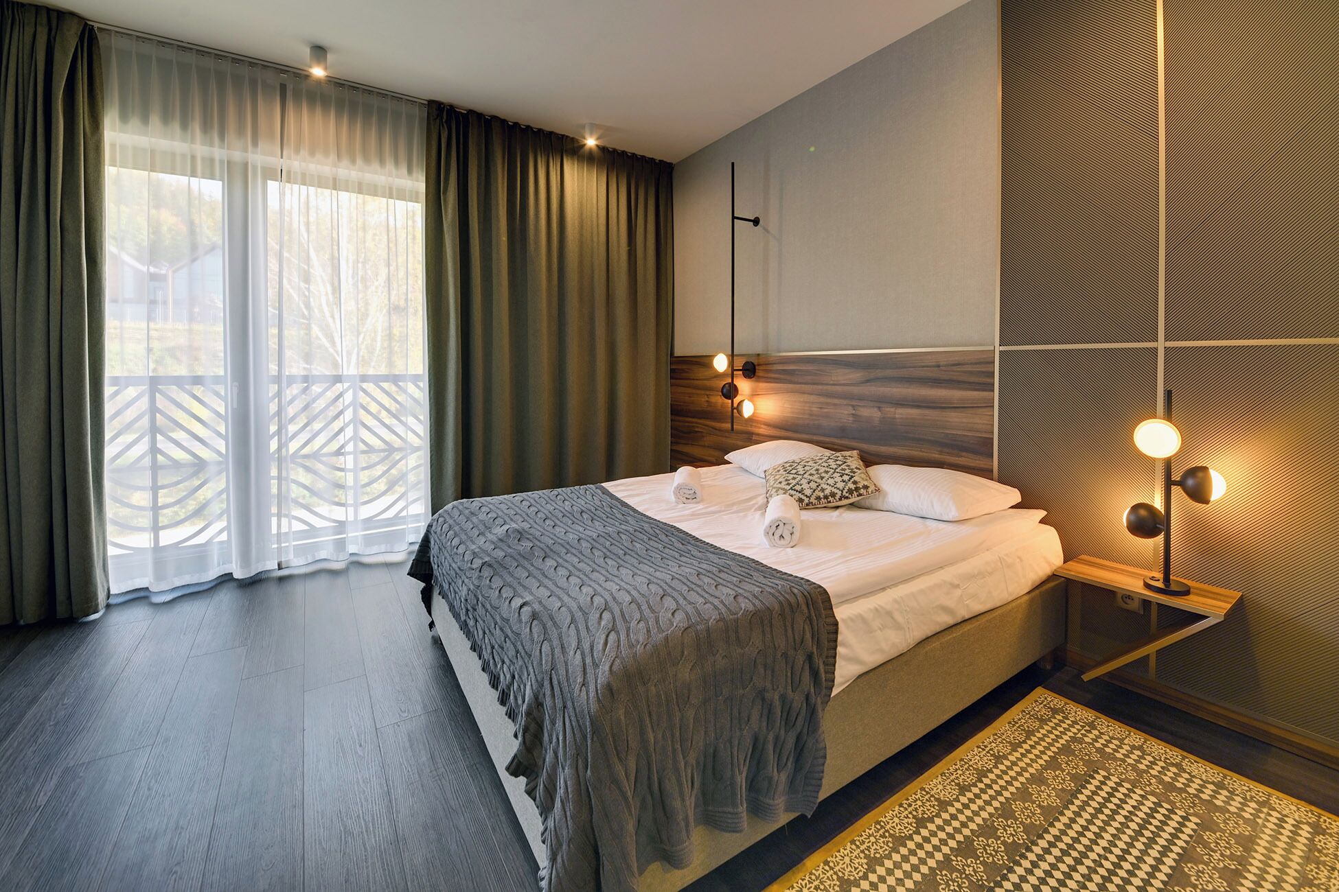 Un dormitorio moderno con una cama grande, cabecera de madera y alfombra estampada.