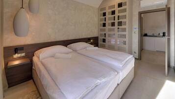 A modern hotel room with a large bed, bedside lamps, a built-in wardrobe, and a kitchenette.