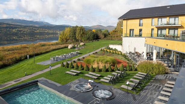Um hotel com piscina, área de estar externa e vista para um lago e montanhas.