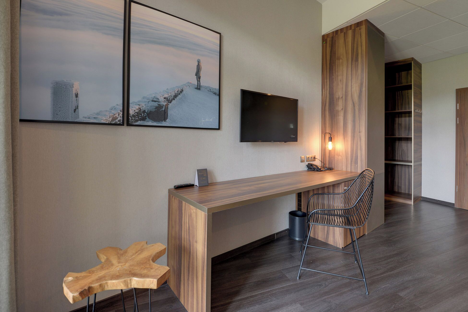 Una camera d'hotel moderna con una scrivania in legno, una TV a parete e un'ampia finestra.