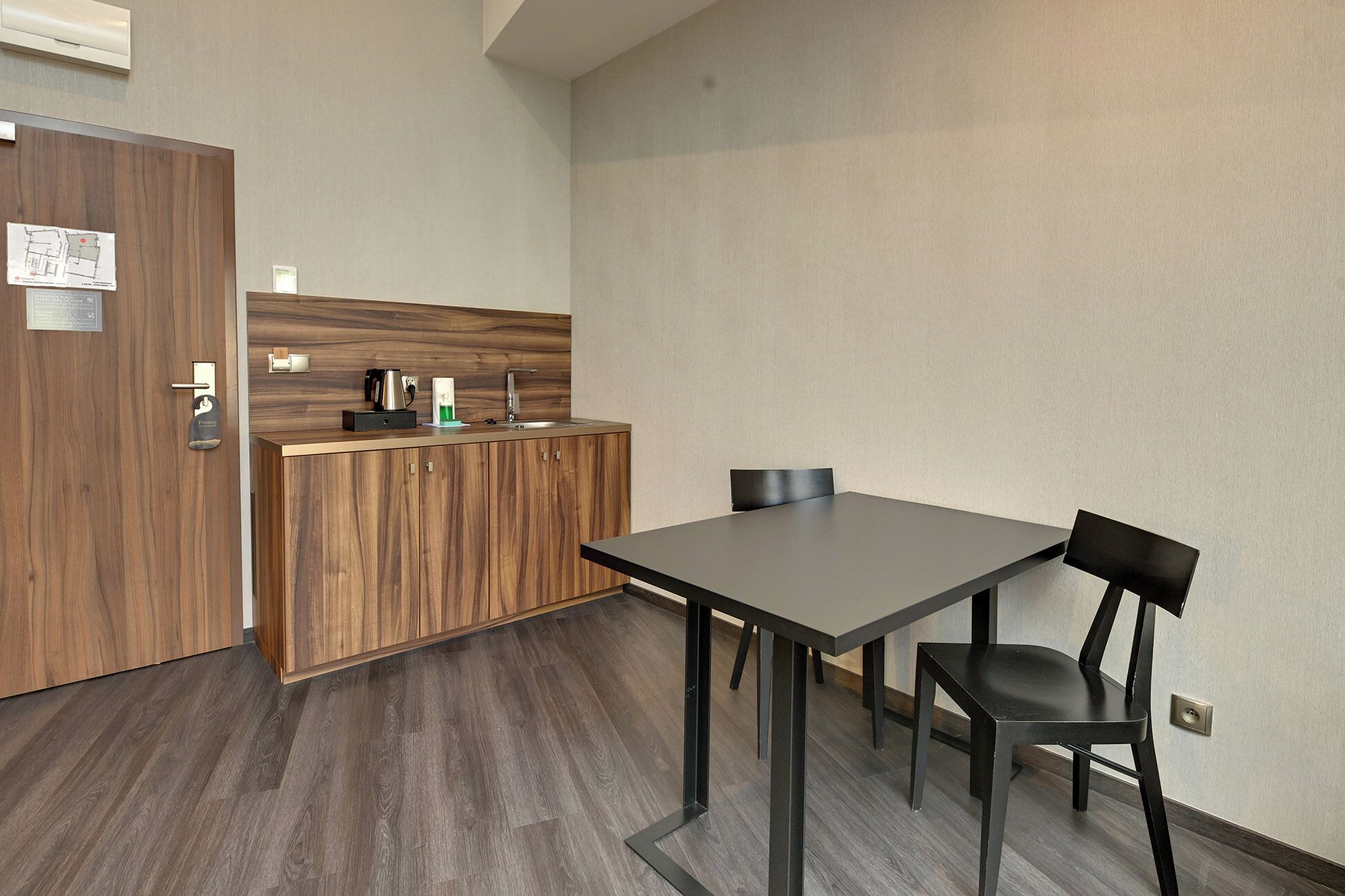 Une petite cuisine moderne, dotée d’un plan de travail en bois, d’une machine à café et d’une bouilloire. La pièce contient une seule chaise et une table.