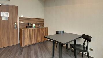 Une petite cuisine moderne, dotée d’un plan de travail en bois, d’une machine à café et d’une bouilloire. La pièce contient une seule chaise et une table.