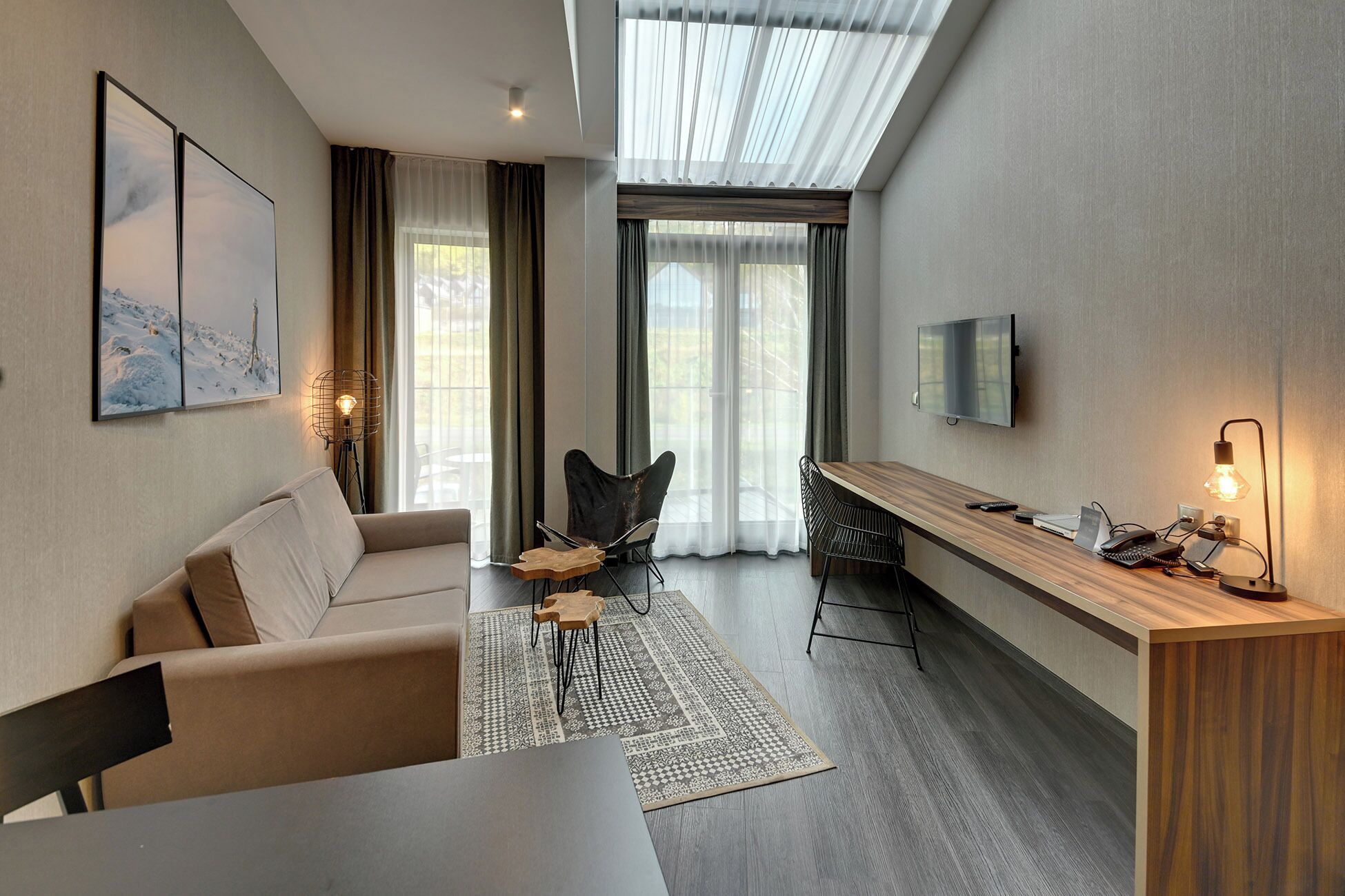 A modern living room with a sofa, a coffee table, a TV mounted on the wall, and a desk with a lamp.