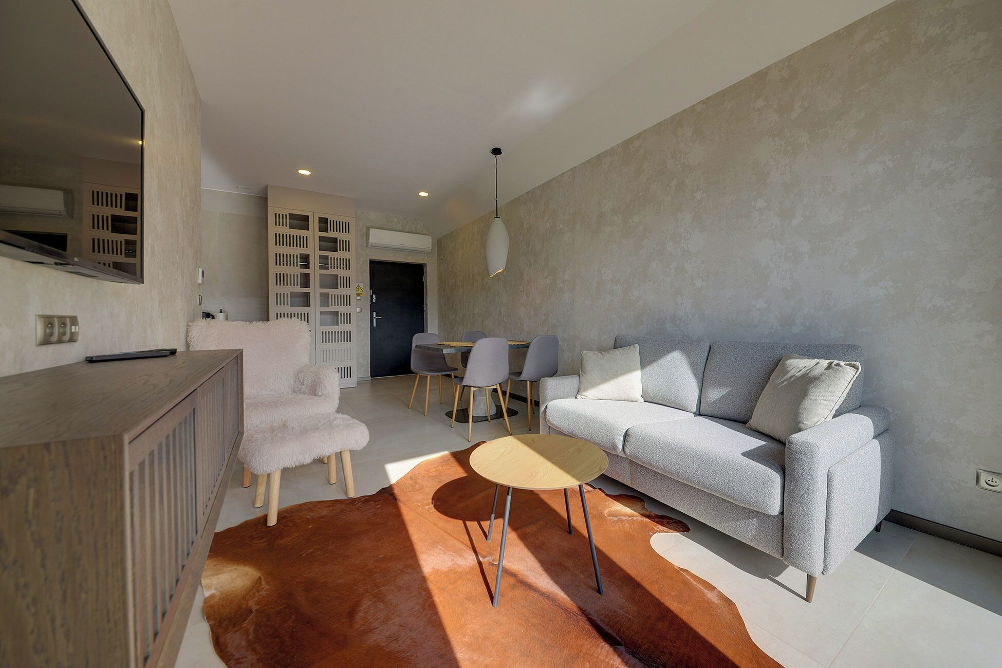 A modern living room with a grey sofa, a wooden coffee table, and a fluffy white chair.