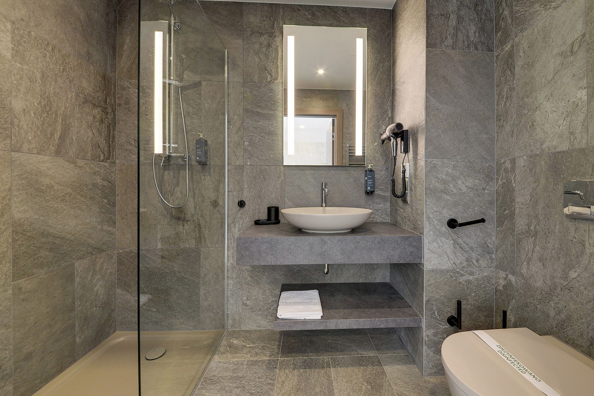 A modern bathroom with a glass-enclosed shower, a pedestal sink, and a toilet.