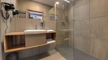 Un bagno moderno con doccia vetrata, mobile contenitore in legno con lavabo e asciugacapelli fissato alla parete.