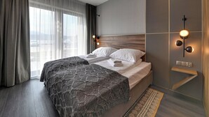 Quarto de hotel moderno com uma cama grande, vista da cidade e luminária fixada na parede.