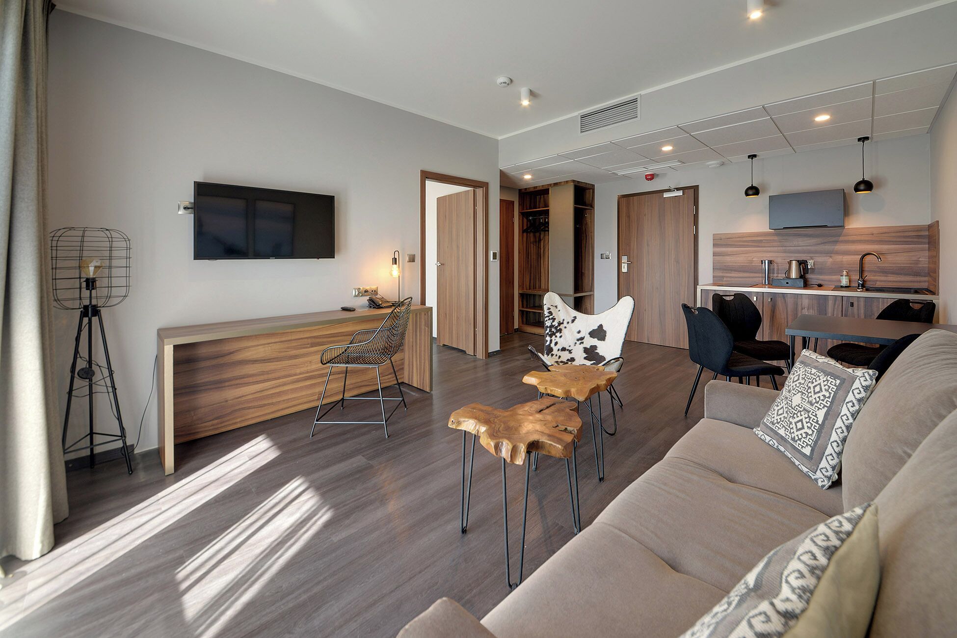 Un salon moderne comprenant un canapé, des fauteuils, une table basse, un téléviseur et un coin cuisine avec une table à manger et des chaises.