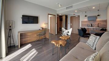 Un salon moderne comprenant un canapé, des fauteuils, une table basse, un téléviseur et un coin cuisine avec une table à manger et des chaises.