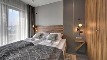 A modern hotel room with a large bed, a wooden headboard, a small seating area, and a view of the outdoors.
