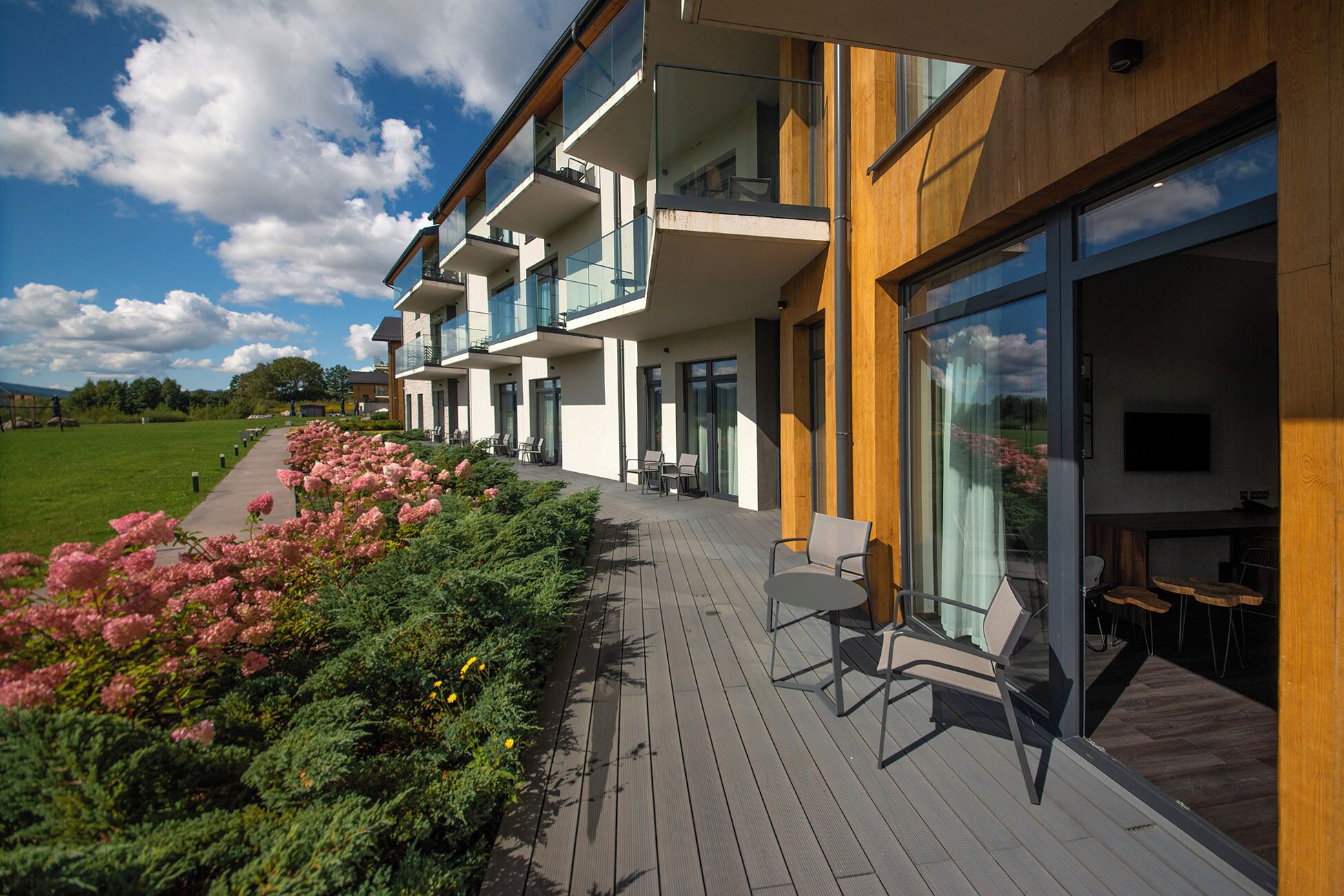 A modern hotel with multiple balconies, outdoor seating, and a view of a green landscape.