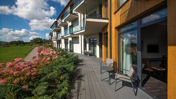 A modern hotel with multiple balconies, outdoor seating, and a view of a green landscape.