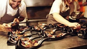 Chefs preparing food in a professional kitchen with stainless steel surfaces and modern equipment.