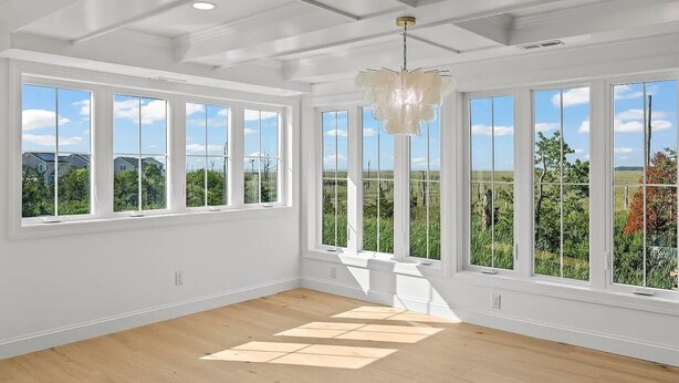 A spacious room with large windows, a chandelier, and a wooden floor.
