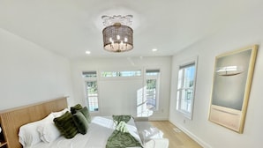 A bedroom with a bed, a bedside table, a chair, a window, and a chandelier.