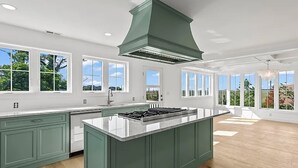 A spacious kitchen with a central island, large windows, and a view of the outdoors.