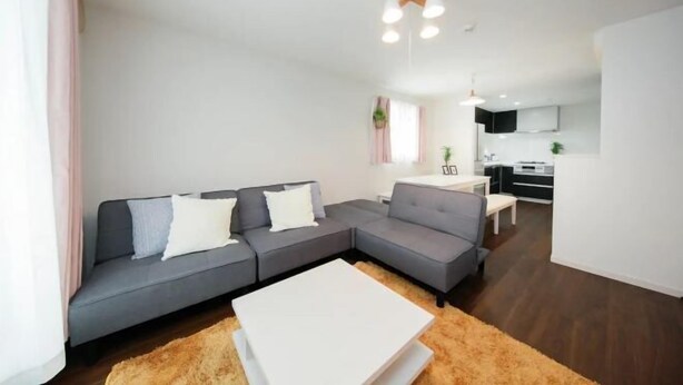 A modern living room with a grey sectional sofa, a white coffee table, and a kitchen in the background. - Higashi Rokugou Black by Tranova (Tokyo)
